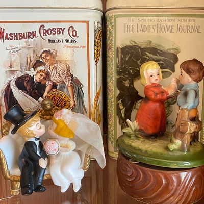 Sale Photo Thumbnail #101: Pair of vintage advertising tins including Washburn Crosby Co. and The Ladies' Home Journal alongside ceramic figurine collectibles.