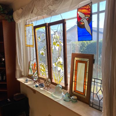 Sale Photo Thumbnail #23: Collection of stained glass window panels featuring floral and bird motifs, displayed along a window sill alongside glass paperweights and decorative items.