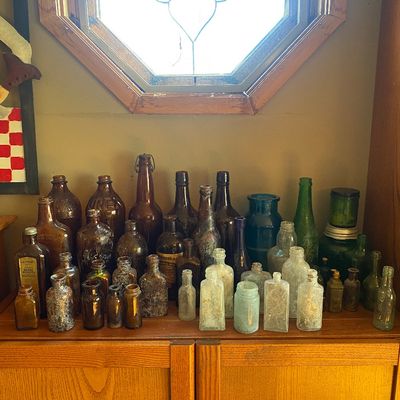 Sale Photo Thumbnail #72: Large collection of antique glass medicine bottles and jars in various shades of amber, clear, teal, and green glass, arranged on a wooden cabinet.