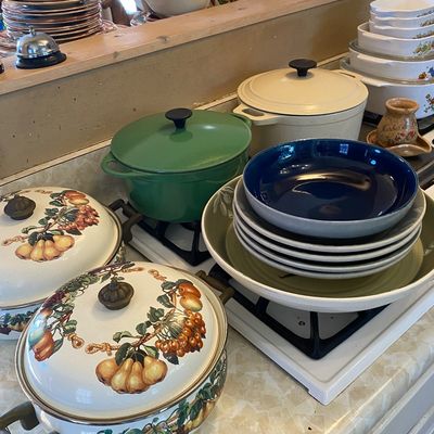 Sale Photo Thumbnail #31: Collection of kitchenware featuring enameled cast iron Dutch ovens, fruit-motif cookware, and stacked ceramic bowls on a counter.