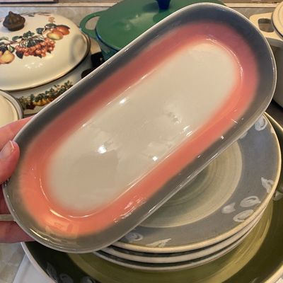 Sale Photo Thumbnail #15: Vintage ceramic oval serving dish featuring a pink and grey glaze design, held above a stack of matching mid-century tableware.