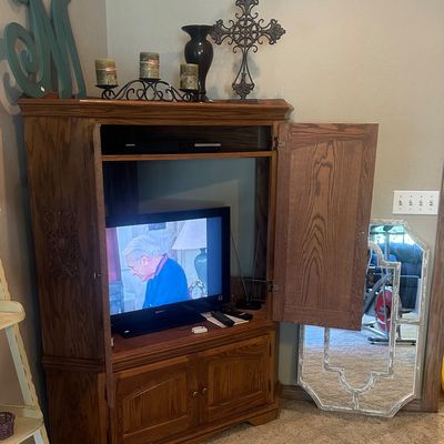 Sale Photo Thumbnail #27: Traditional oak media armoire featuring carved details, lower cabinet storage, and pocket doors, displayed with decorative home accents.
