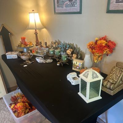 Sale Photo Thumbnail #25: Display table featuring autumn-themed home decor, including faux floral arrangements, decorative candles, a white metal lantern, framed wall art, and a table lamp.