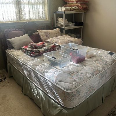 Sale Photo Thumbnail #55: Wooden bed frame with floral quilted mattress, set up with assorted throw pillows, folded quilts, and clear plastic storage bins in a bedroom.
