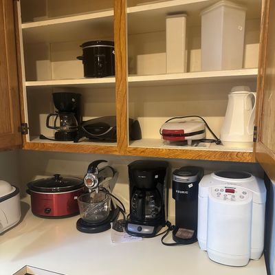 Sale Photo Thumbnail #37: Collection of small kitchen appliances, including coffee makers, slow cookers, a Keurig, a stand mixer, and a bread maker, displayed on a countertop and in open cabinets.