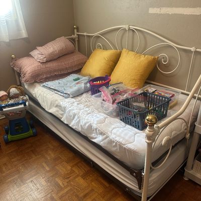 Sale Photo Thumbnail #64: White metal scrollwork daybed with brass finials and trundle frame, loaded with bedding and plastic storage bins containing small toys.