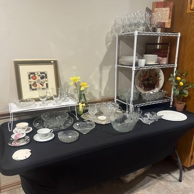 Sale Photo Thumbnail #41: Collection of vintage cut glass and crystal glassware, teacups, and serving pieces displayed on a table alongside framed wall art and a white shelving rack.