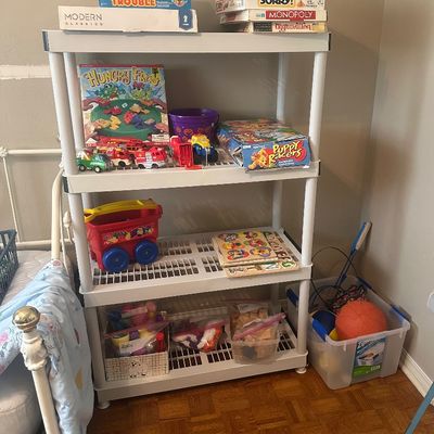 Sale Photo Thumbnail #62: White plastic four-tier shelving unit filled with vintage board games, toy vehicles, wooden puzzles, and crafting supplies.