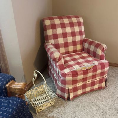 Sale Photo Thumbnail #29: Red and cream buffalo check upholstered armchair with heavy wear and tearing on the seat cushion and arm, set next to a cream wire magazine basket.