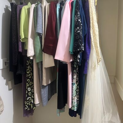 Sale Photo Thumbnail #57: Collection of vintage women's clothing hanging on a closet rack, including colorful jackets, dresses, prints, and a lace wedding dress with a veil.