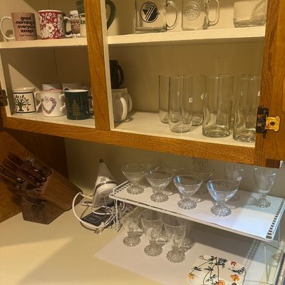 Sale Photo Thumbnail #47: Assorted kitchen glassware and ceramic mugs arranged inside an open wooden cabinet and on a countertop organizer shelf.