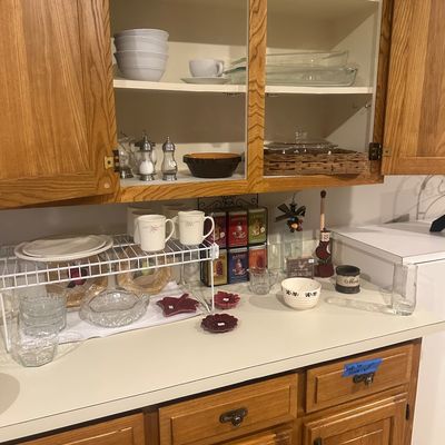 Sale Photo Thumbnail #34: Kitchen cabinet and countertop array featuring white dishes, clear glass serveware, mugs, tea tins, and various small decorative tableware items.