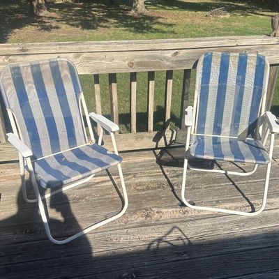 Sale Photo Thumbnail #21: Pair of vintage folding lawn chairs featuring white tubular metal frames and blue and white striped mesh fabric, showing moderate signs of wear.