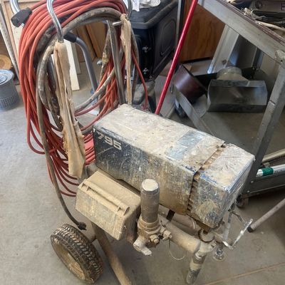 Sale Photo Thumbnail #18: Heavy-duty Graco Ultra Max 795 airless paint sprayer on a wheeled cart, showing heavy cosmetic wear and paint residue, with a coiled orange power extension cord.