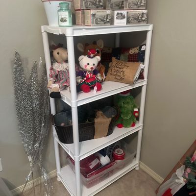 Sale Photo Thumbnail #44: White plastic four-tier shelving unit display filled with holiday decor, plush toys, boxed collectibles, and decorative pillows.