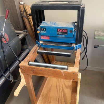 Sale Photo Thumbnail #16: Vintage Ryobi 10-inch surface planer mounted on a custom wooden stand, showing typical workshop wear and sawdust.