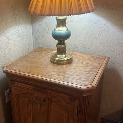 Sale Photo Thumbnail #46: Traditional brass and blue ceramic table lamp with a pleated shade, set atop a 1980s oak side cabinet with double doors.