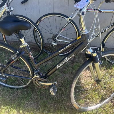 Sale Photo Thumbnail #14: Giant Eddie Bauer EB Spirit hybrid bicycle with a dark metallic frame, front suspension, and padded saddle, shown alongside other road bikes.