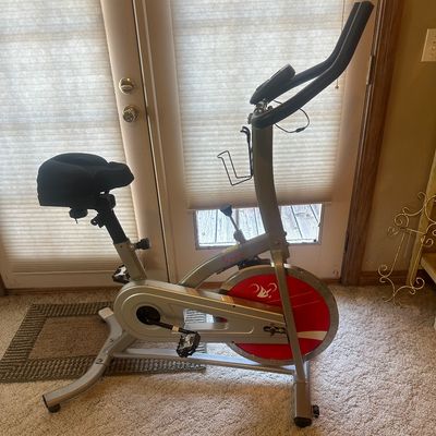 Sale Photo Thumbnail #28: Sunny Health & Fitness stationary exercise bike with a cushioned seat cushion, water bottle holder, and red flywheel accent.
