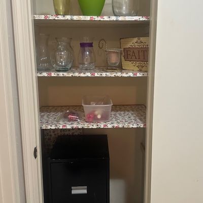 Sale Photo Thumbnail #49: Open closet featuring floral-lined shelves filled with glassware, decor, and a black two-drawer filing cabinet at the bottom.