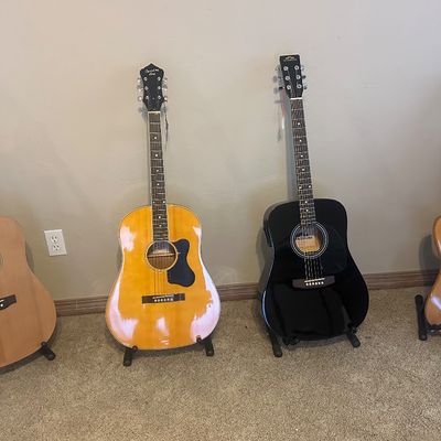 Sale Photo Thumbnail #3: Collection of four guitars on floor stands, including three acoustic models and one natural-finish electric Stratocaster-style guitar.