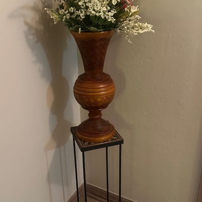 Sale Photo Thumbnail #50: Carved wooden floor vase filled with faux lavender and white floral stems, displayed on a wrought iron plant stand.