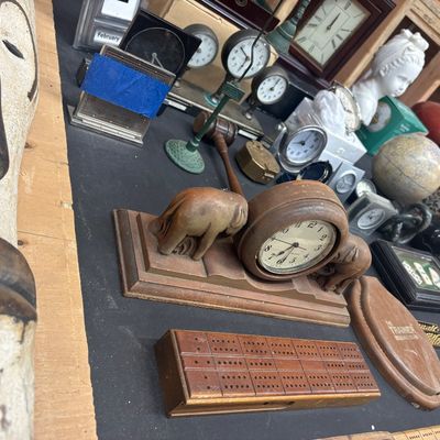Sale Photo Thumbnail #9: Collection of vintage desk accessories, small clocks, and carved wooden decor items including a wooden elephant clock and cribbage boards displayed on a table.