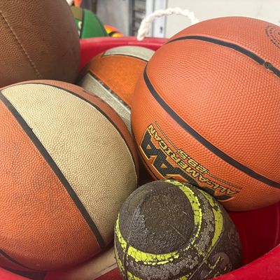 Sale Photo Thumbnail #26: Collection of used sports balls, including an NCAA All-American basketball, leather footballs, and playground balls stored in a red plastic bin.