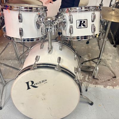 Sale Photo Thumbnail #39: Vintage Rogers white drum kit with bass drum, two mounted rack toms, chrome hardware, and attached Zildjian cymbal on a stand.