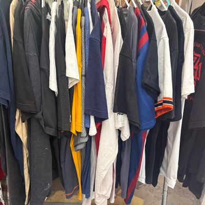 Sale Photo Thumbnail #2: Clothing rack densely filled with assorted men's casual shirts, including graphic t-shirts, polo shirts, and long-sleeve tops in various colors.