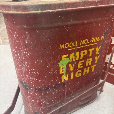 Sale Photo Thumbnail #28: Vintage red metal oily rag safety can, model no. 906-FL, featuring stencil lettering reading "EMPTY EVERY NIGHT." Displays a distressed finish with paint splatters, surface rust, and patina.