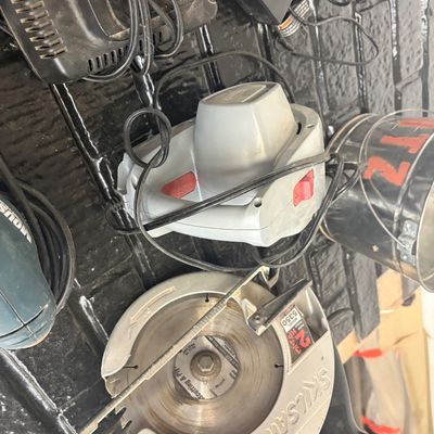 Sale Photo Thumbnail #47: Vintage Skilsaw model 5350 corded circular saw alongside a grey handheld power tool and various power cords.