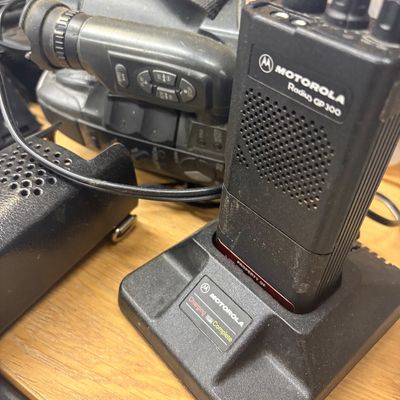Sale Photo Thumbnail #4: Vintage Motorola Radius GP300 two-way radio sitting in a charging base, alongside a Panasonic camcorder.