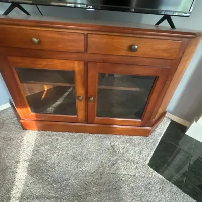 Traditional cherry-finish wood corner media console featuring two top drawers and lower glass-paneled cabinet doors.