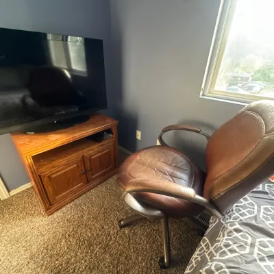 Brown leather executive office chair on casters alongside a wooden TV media stand and flat-screen television.