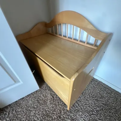 Light oak wooden toy chest with an arched spindled backrest, bench seating, and safety cutout handle.