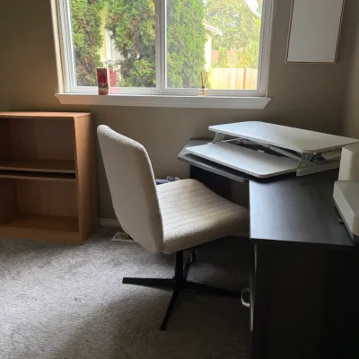 Dark L-shaped corner desk with a white standing desk converter, paired with a light cream upholstered swivel task chair.