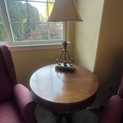 Traditional round Grand Rapids mahogany side table with a pedestal base, accompanied by a scrollwork metal table lamp.