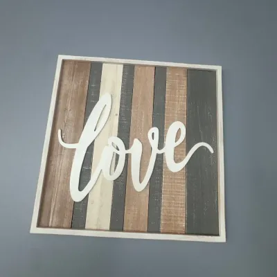 Rustic farmhouse-style framed wooden wall art featuring a cut-out script "love" overlay on vertical multi-toned wood planks.