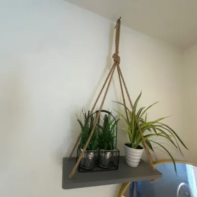 Hanging gray wooden wall shelf suspended by jute rope, holding potted artificial plants.