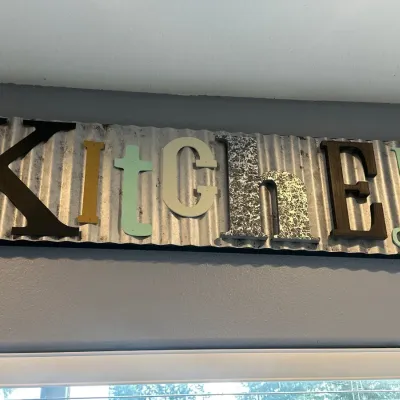 Rustic wall sign reading 'Kitchen' featuring mixed-style letters mounted on a corrugated galvanized metal panel.