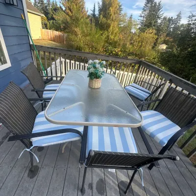 Outdoor patio dining set featuring a rectangular glass-top table and six dark metal mesh armchairs with blue and white striped seat...