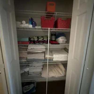Linen closet filled with assorted folded towels, bed sheets, small appliances, and woven storage baskets.