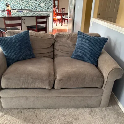 Contemporary beige microfiber loveseat with rolled arms, paired with two blue textured throw pillows.