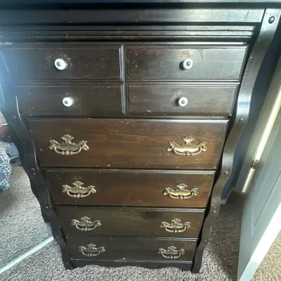Dark stained wood tall chest of drawers featuring white knobs on top drawers and brass bale handles on bottom drawers.