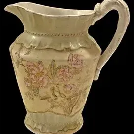 Antique ironstone water pitcher featuring hand-painted pink floral motifs and molded ruffled detailing.