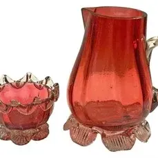Vintage ruby red pressed glass cream pitcher and open sugar bowl set featuring clear glass handles and bases.