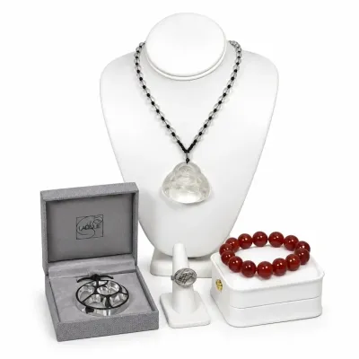 Sale Photo Thumbnail #12: Collection of fine designer jewelry featuring a frosted glass Laughing Buddha pendant necklace, a red carnelian bead bracelet, a silver-toned oval ring, and a modern silver geometric pendant in its original grey Lalique presentation box.