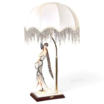 Sale Photo Thumbnail #184: Art Deco style Giuseppe Armani table lamp featuring a figurine of a flapper woman in a silver dress with a peacock, topped with a white dome shade accented by beaded fringe.