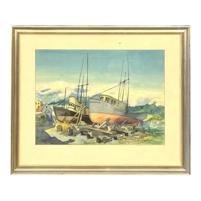 Sale Photo Thumbnail #35: Framed original watercolor painting depicting drydocked fishing boats in a coastal harbor, presented with a cream mat in a gilt wooden frame.